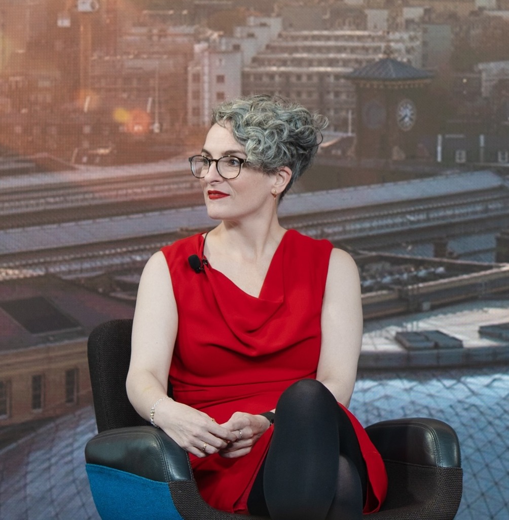 Kelly Webb-Davies speaking in red dress